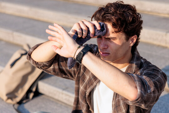 Man wiping forehead and shielding eyes on steps in hot weather