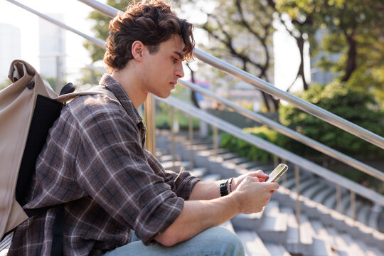 Young man with backpack using phone on outdoor steps.