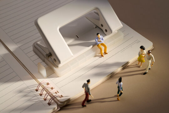 Miniature people interacting around a hole puncher on a lined notebook