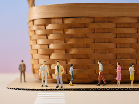 Miniature people standing in front of a large woven basket