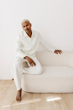 Man posing sitting on sofa in white suit