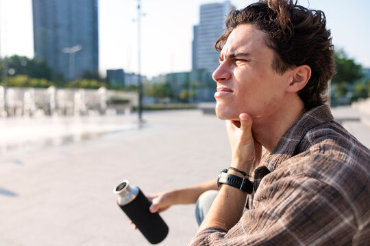 Man squinting in scorching sunlight holding water bottle in city