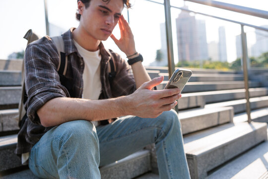 Worried man on steps looking at mobile phone.