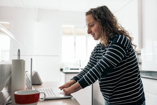 Woman with disability typing a laptop in kitchen