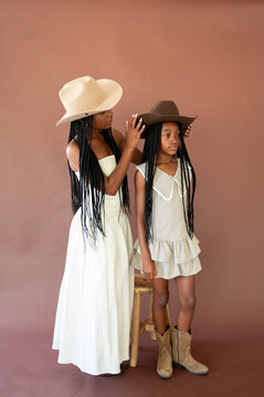 Mother Helps Daughter Try on Cowboy Hat in Studio Setting