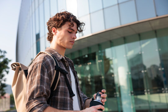 Man opening water bottle in urban heat near modern building