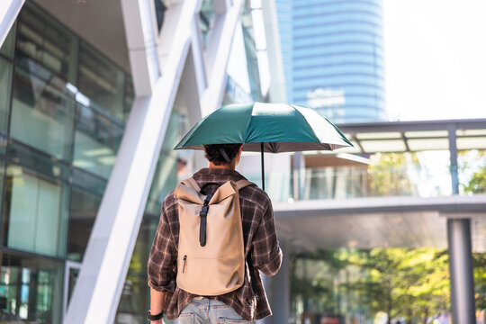 Man with backpack and umbrella walks in city.