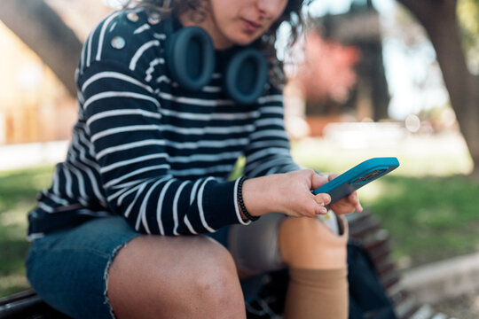 Woman with prosthetic leg using smartphone in park
