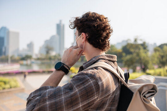 Masked traveler with backpack views city skyline.