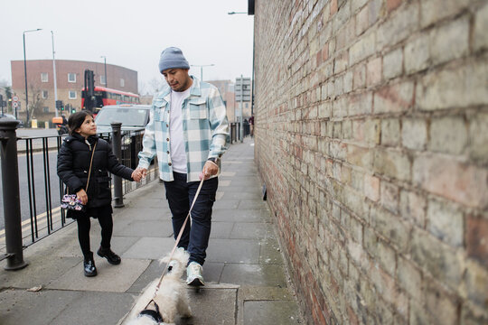 Father and daughter walking dog on city sidewalk interacting together