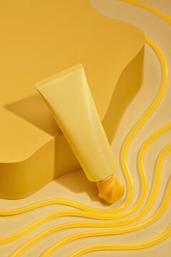 Minimalist yellow cosmetic tube with product on yellow podium