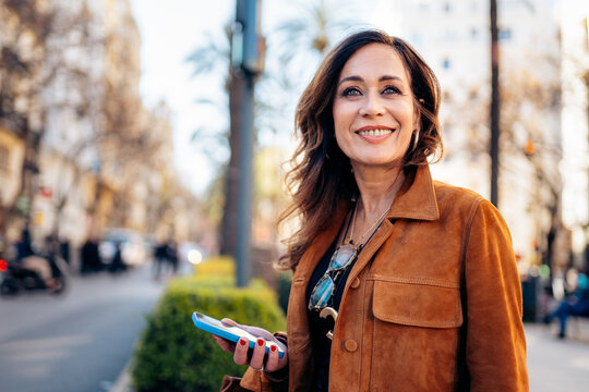 Mature woman smiling holding smartphone outdoors in city
