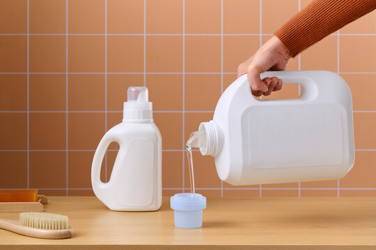 Pouring liquid detergent from a large bottle into a smaller cap