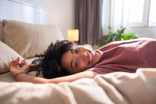 Smiling woman relaxes in bed on a sunny morning.