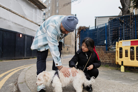 Father and daughter petting dog on city street
