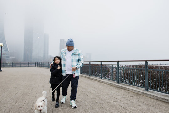 Father embracing daughter walking dog on foggy city promenade