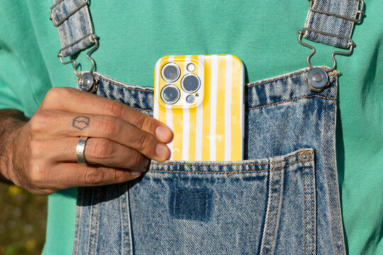 Man Holds Phone in Pocket of Denim Overalls 