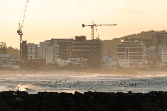 Surfers in the ocean with coastal construction and cranes at sunset