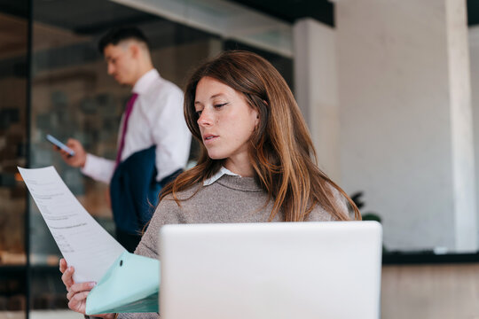 Woman Reviewing Documents While Man Uses a Phone in Office