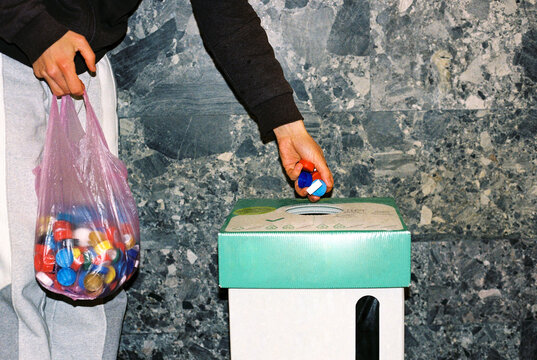  Male's volunteer throwing bottle caps into a container.