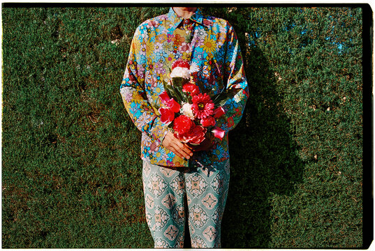 a man holds a bright bouquet against a green hedge, 35mm film