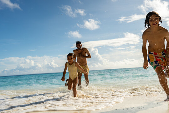 Father chasing children from ocean waves on tropical beach