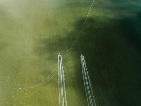 Two boats leaving wakes on shallow lagoon water, drone view