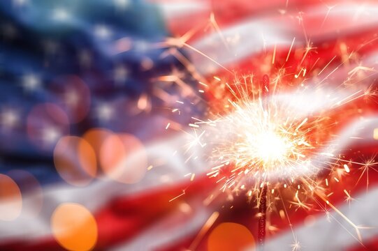 Sparkler burning against a blurred American flag background for Independence Day