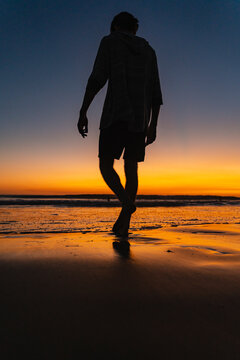 Man walking barefoot on beach at sunset