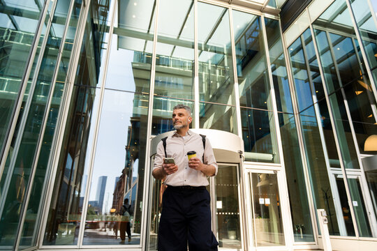 Businessman Leaving Office Holding Phone And Hot Drink