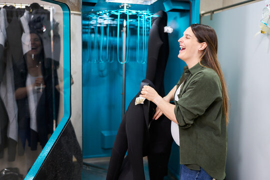 Happy woman handling wetsuit in dive center drying machine