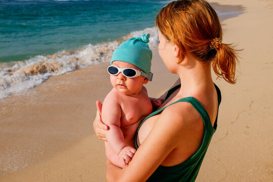 Mother holding baby in sunglasses on sunny beach