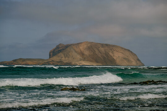 Island stands near shore with waves crashing at its base