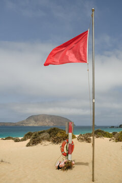 Red flag flying at beach with lifebuoy and mountain view