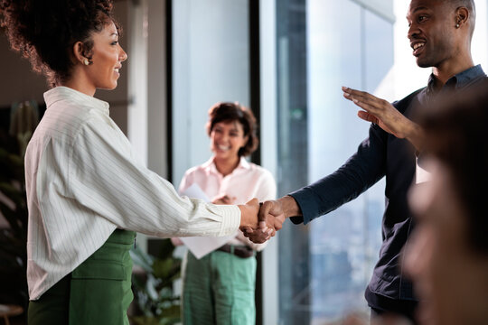 Business people shaking hands, colleague smiling in background.