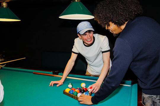 Friends enjoying billiards game, laughing and setting up for play