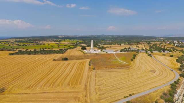 Seddulbahir, Eceabat, Turkey. Helles Memorial obelisk, a 30-meter limestone monument rising from golden Gallipoli fields, aerial drone view over the Dardanelles Strait under clear summer skies. Aeria