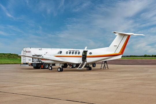 Air ambulance plane with open door parked on airport tarmac under cloudy sky.