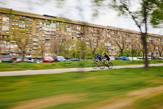 Two Cyclists Ride on a Path Beside a Large Building