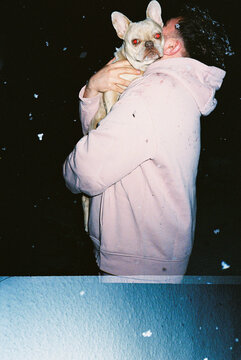 Man holding French bulldog in falling snow at night