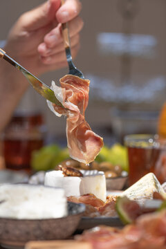 Delicious Italian ham slice held by fork and knife over appetizers