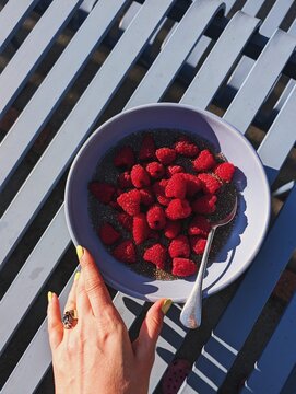 Hands Holding a Bowl of Raspberries and chia seeds, Blue Table Surface
