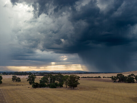 Heavy rain falling from dramatic storm clouds on farmland at sunset