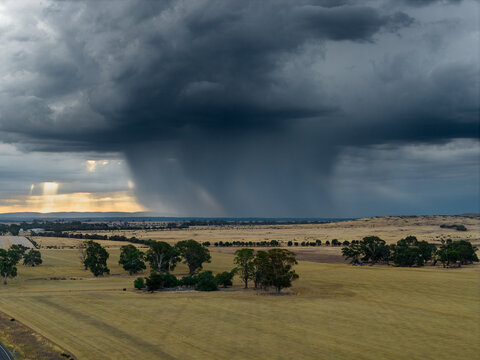 Heavy rain falling from dramatic storm clouds on farmland at sunset