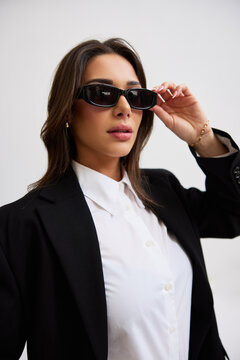 Woman wearing sunglasses in a black suit posing indoors