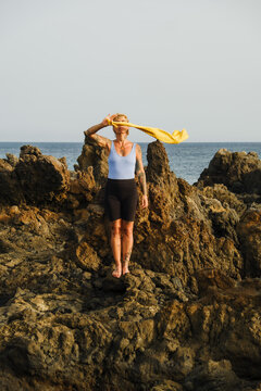 Standing on rocks by the sea with a yellow scarf in the wind
