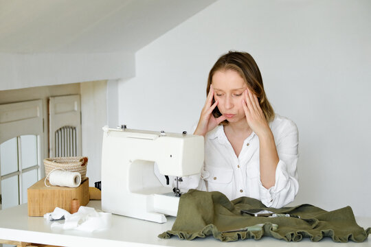 A woman stressing and  sitting close to a sewing machine.