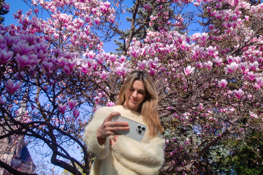 A woman taking selfies in front of a cherry blossom tree