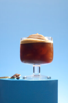 Refreshing iced coffee with creamy foam and coffee beans on blue
