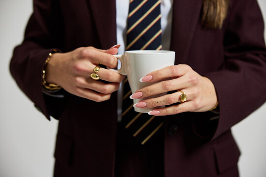 Woman holding cup in formal outfit with jewelry in indoor settin